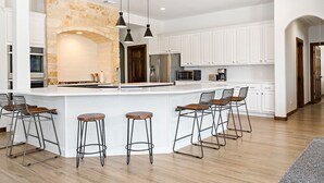 Een moderne keuken met een centraal eiland, barkrukken, witte kastjes en een accentmuur van steen.