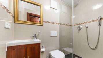 A modern bathroom with a wooden vanity, a toilet, a shower with a glass door, and a mirror with a gold frame.