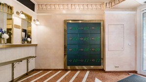 Un hall d’hôtel doté d’un sol en marbre, d’un comptoir de réception avec un miroir, d’appliques murales et d’un grand coffre-fort numéroté.
