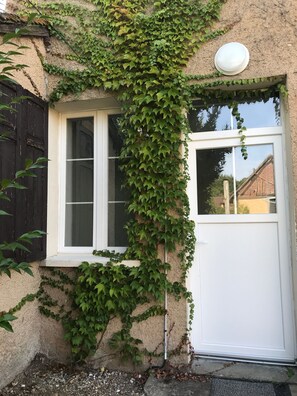 Um edifício com porta e janela brancas, parcialmente coberto por hera verde.