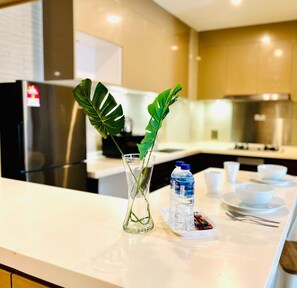 A modern kitchen with a white countertop, a glass vase with a plant, and a tray with water bottles and snacks.