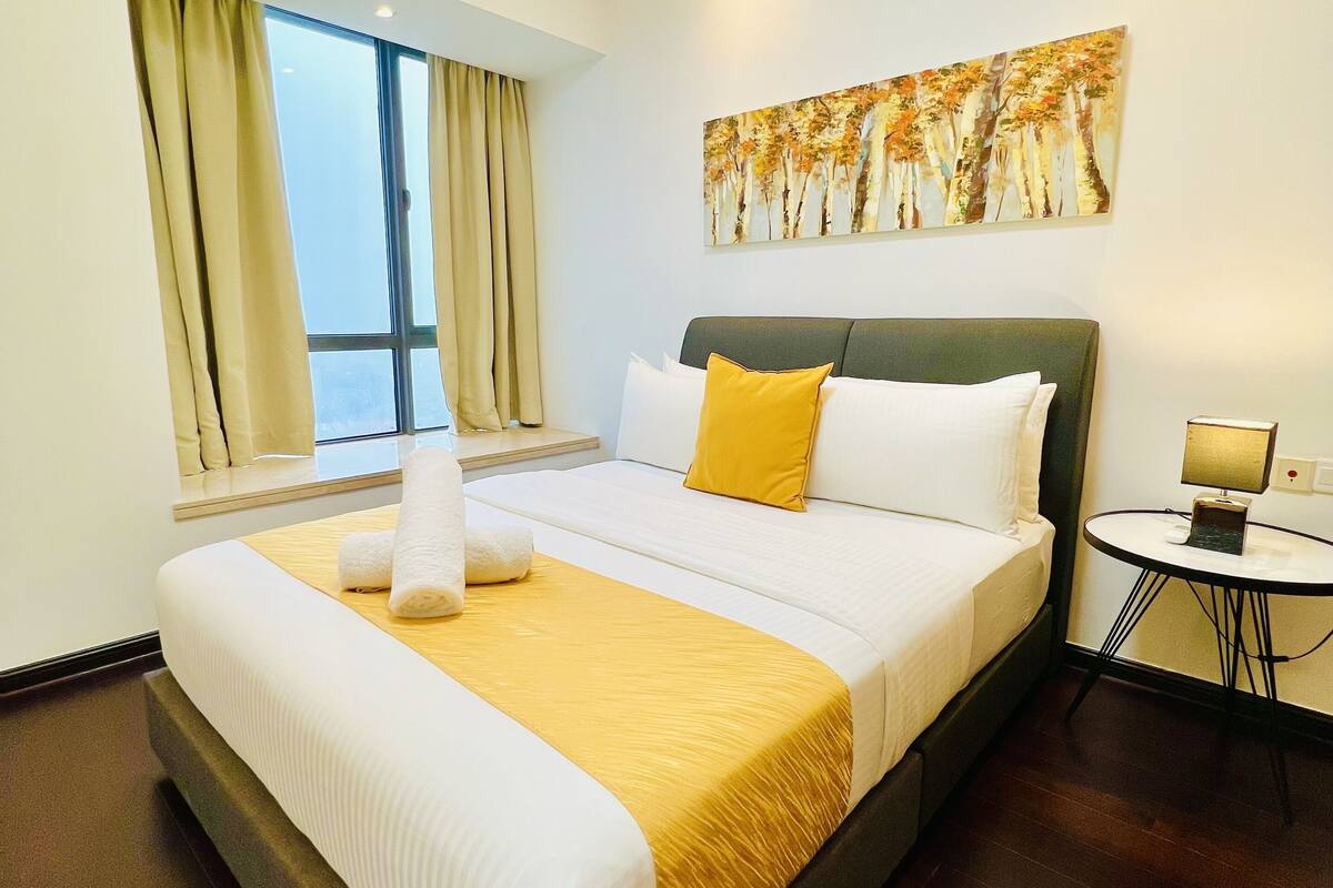 Een hotelkamer met een groot bed, een klein rond tafeltje, een raam met gordijnen en een schilderij aan de muur.