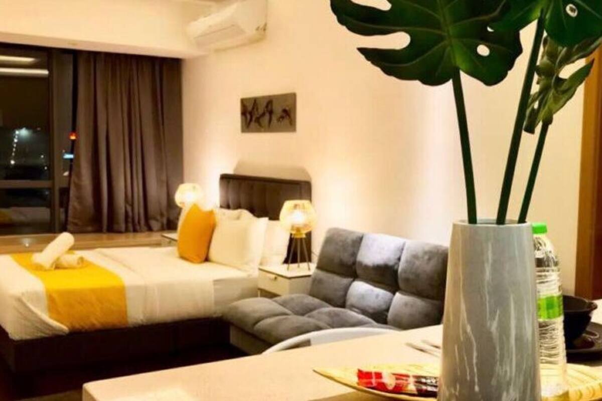 Een hotelkamer met een bed, een bank, een eettafel, een grote plant en een raam met gordijnen.