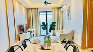 A modern dining area with a long table set for six, a white sofa, and a large window with curtains. - R&F PRINCESS COVE BY HOMEFORT SUITES (Johor Bahru)