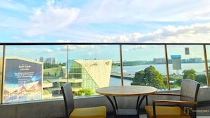 A balcony with a round table and two chairs, overlooking a river and modern buildings. - R&F PRINCESS COVE BY HOMEFORT SUITES (Johor Bahru)