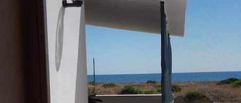 A balcony with a view of the sea, a white wall, and a door.