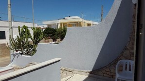 A courtyard with a white wall, a white chair, and a cactus plant. - Appartamento Lido Marini (Ugento)