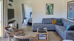 Un soggiorno moderno con un divano grigio, poltrone in vimini, un tavolino in vetro e opere d'arte alle pareti.