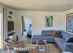 A modern living room with a grey sofa, wicker chairs, a glass coffee table, and artwork on the walls.