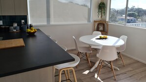 Una cucina moderna con un piano di lavoro nero, un tavolo da pranzo bianco e sedie. Sul piano di lavoro c'è una ciotola di limoni, una pianta pensile e una finestra con vista all'esterno.