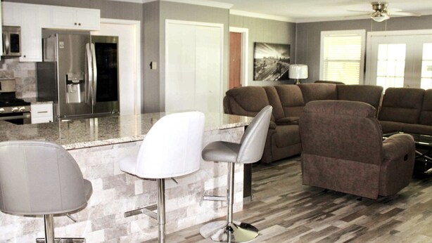 A modern kitchen with a refrigerator, microwave, and stove. There is a bar area with two stools and a couch in the living room. - CYC Lounge with Guest House (San Antonio)