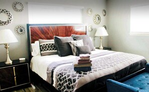 Una cama bien tendida con una colcha estampada, dos lámparas de noche y decoración en la pared.
