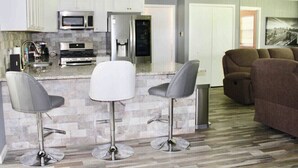 A modern kitchen with a central island, bar stools, and a brown sofa in a living area. - CYC Lounge with Guest House (San Antonio)