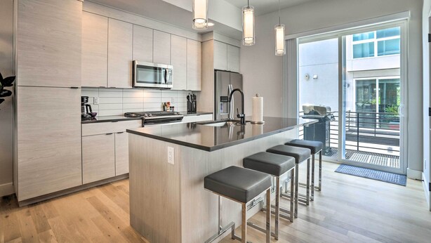 Una cocina moderna con una isla central, taburetes de bar, microondas y refrigerador.