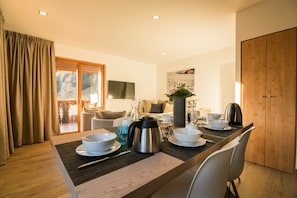 Uma sala de jantar com mesa de madeira, cadeiras brancas e uma cafeteira.
