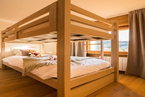 Uma cama de beliche com estrutura de madeira, uma mesa de cabeceira com abajur e uma janela com cortinas.