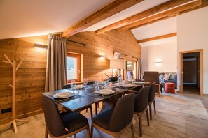 Un comedor con una mesa de madera dispuesta para seis personas, un sofá y un reposapiés rojo en una habitación con paredes de madera y techo inclinado.