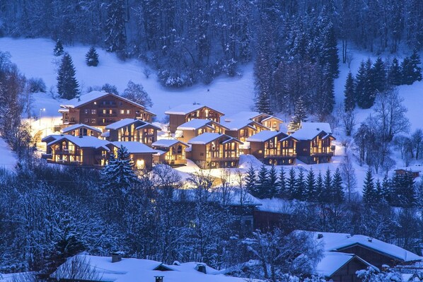 A lodge with multiple wooden buildings, surrounded by snow-covered trees and a snowy landscape.