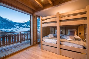 Quarto com beliche de madeira e vista para uma paisagem nevada de montanhas.
