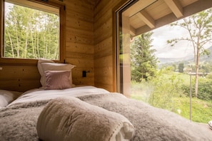 Une chambre dans une cabane en bois, avec un lit, des oreillers et une fenêtre donnant sur un paysage boisé.