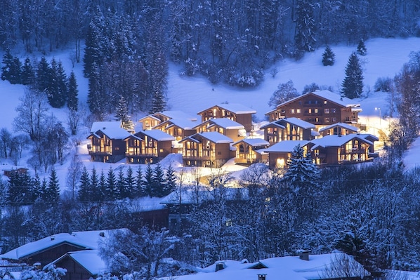 Un ensemble de chalets en bois à plusieurs étages, entourés d’arbres couverts de neige et dominant un paysage montagneux.