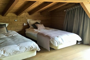 A bedroom with two beds, wooden ceiling beams, a window with curtains, and a wall-mounted light switch. - Megève Chalet w/ Fireplace (Praz-sur-Arly)