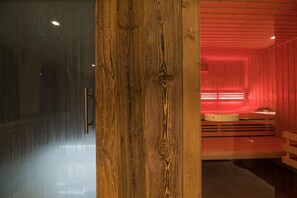 A wooden interior with a glass wall, a wooden column, and a red-lit room with a circular seating area. - Megève Chalet w/ Fireplace (Praz-sur-Arly)