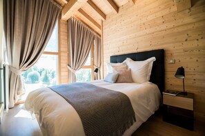 Quarto com painéis de madeira, uma cama, cortinas, uma mesa de cabeceira e uma janela.