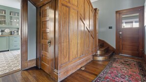 A wooden staircase leading to a second floor, a wooden door, and a kitchen area with cabinets and a patterned rug. - The Arabella House - Charmed Victorian in Historic Downtown Ventura (Ventura)