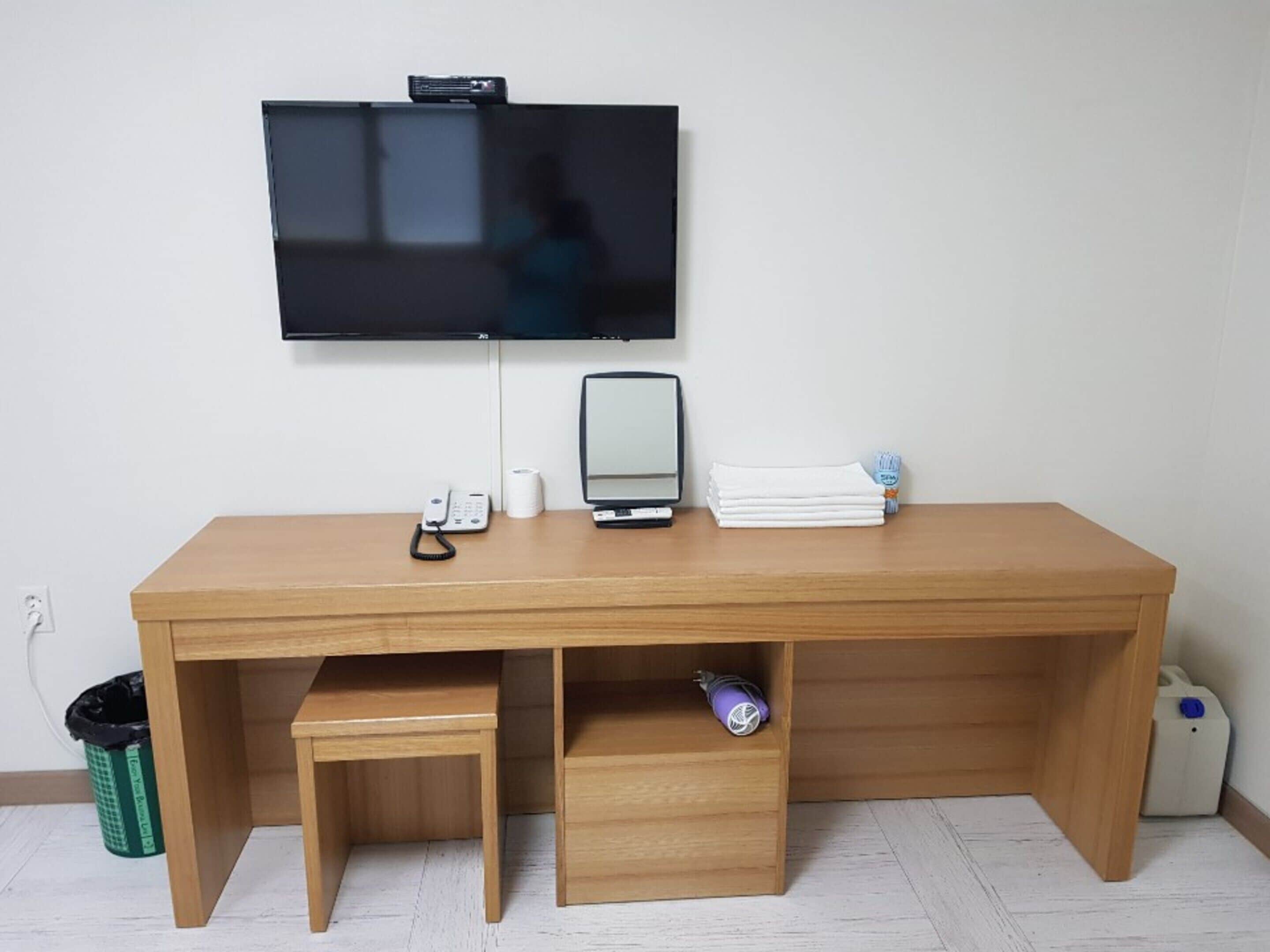 Una taula de fusta amb un televisor de pantalla plana, un telèfon i un ordinador portàtil.