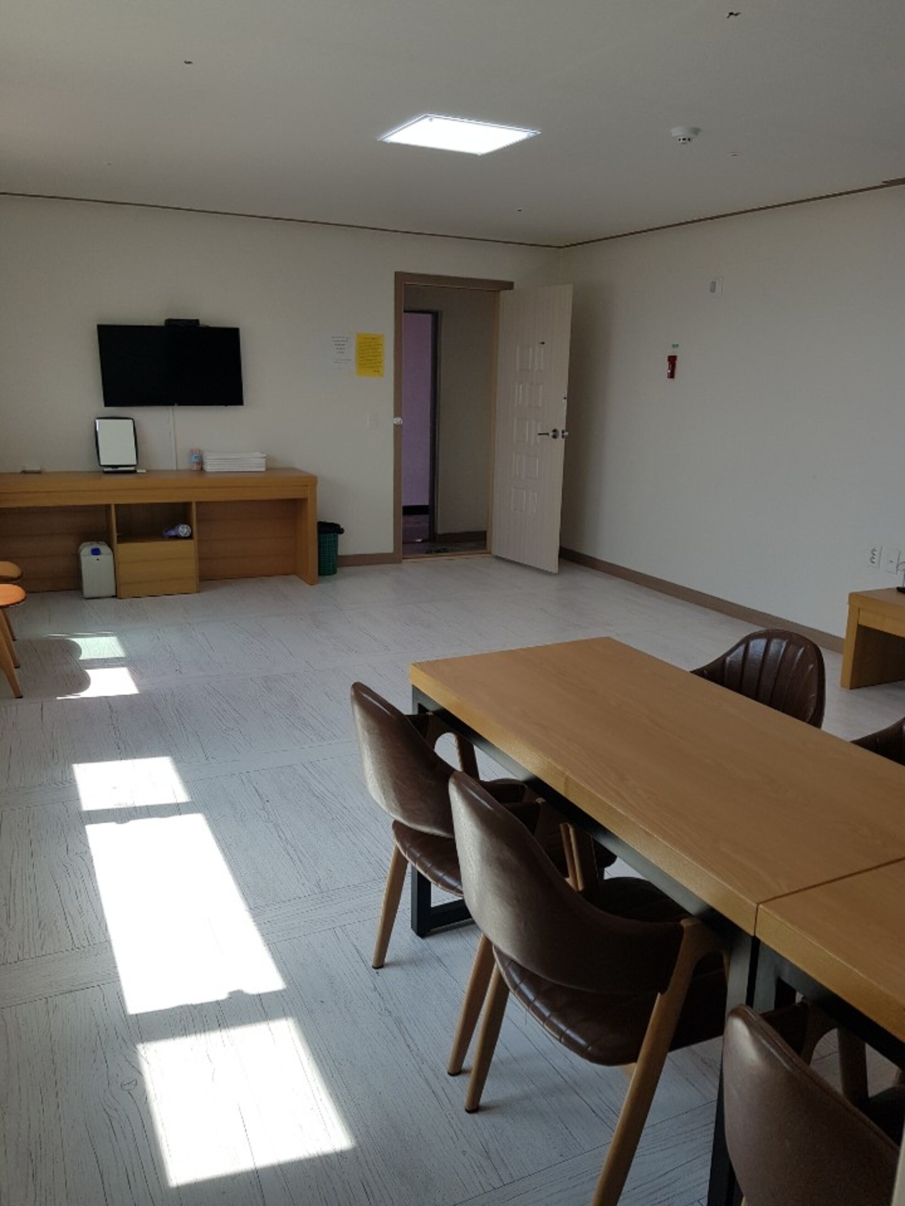 A conference room with a long table, chairs, a desk with a computer, and a television on the wall.