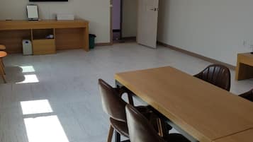 Ein Konferenzraum mit einem langen Tisch, Stühlen, einem Schreibtisch mit Computer und einem Fernseher an der Wand.