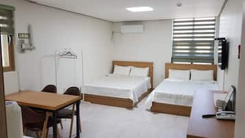 A hotel room with two beds, a desk, and a chair. There is a window with blinds, a TV mounted on the wall, and a small table with a kettle.