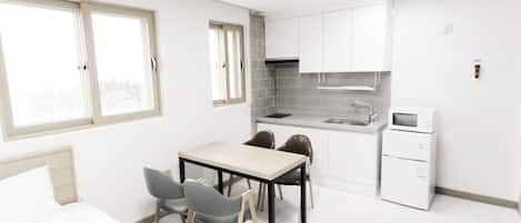Una cocina compacta con armarios blancos, un fregadero y un microondas. Hay una zona de comedor con una mesa y sillas.