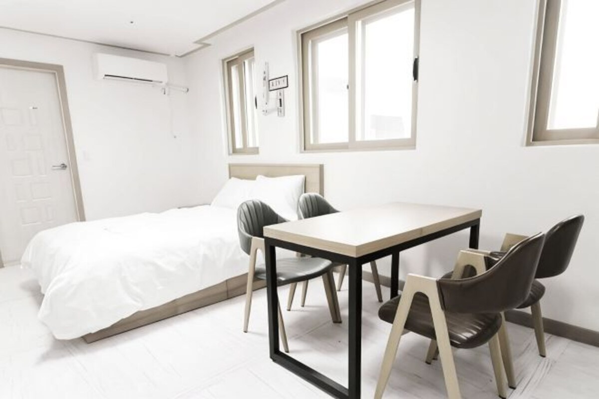 A bedroom with a bed, a desk, two chairs, and a window.