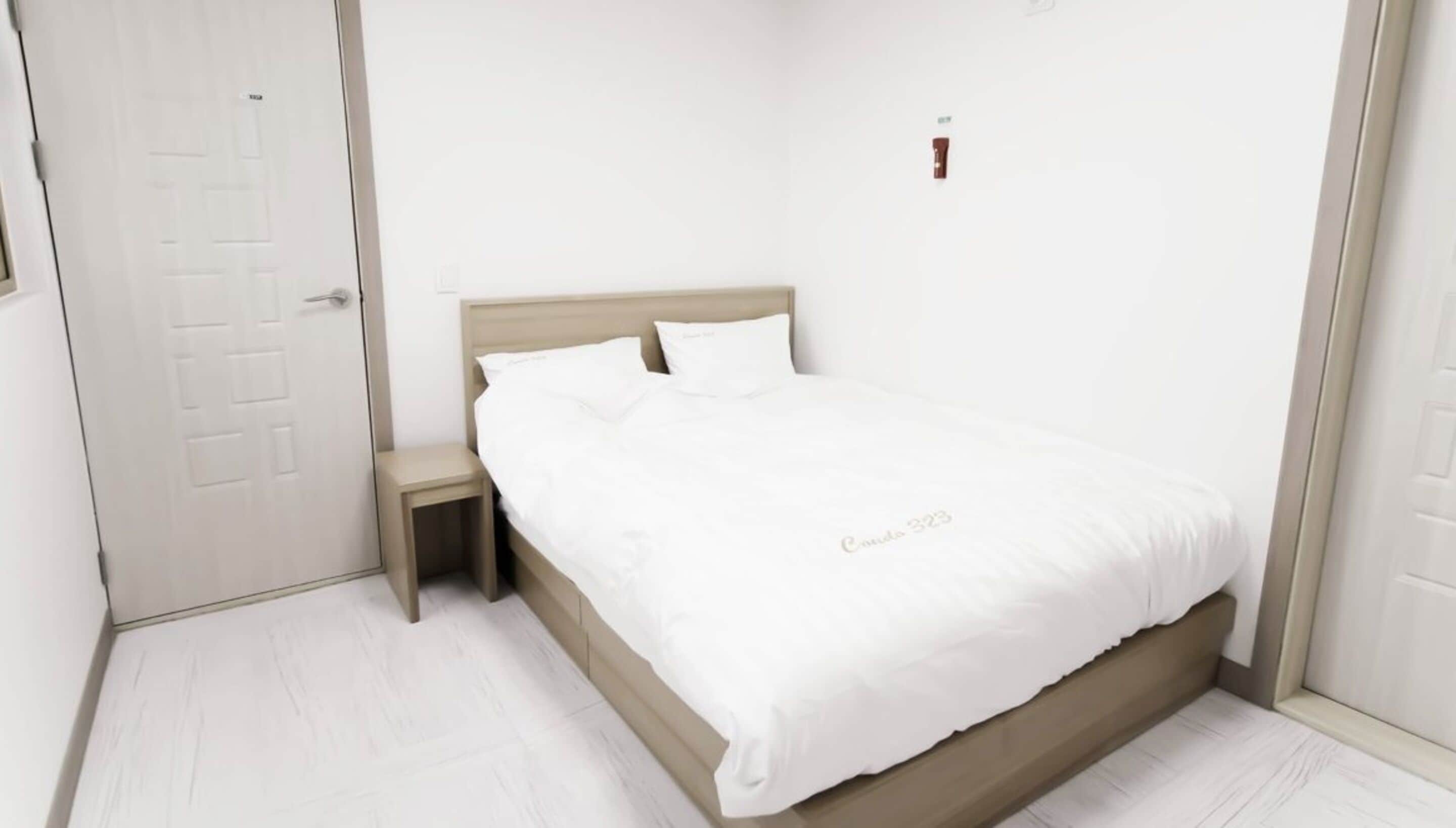 Quarto minimalista com cama, mesa de cabeceira e porta.