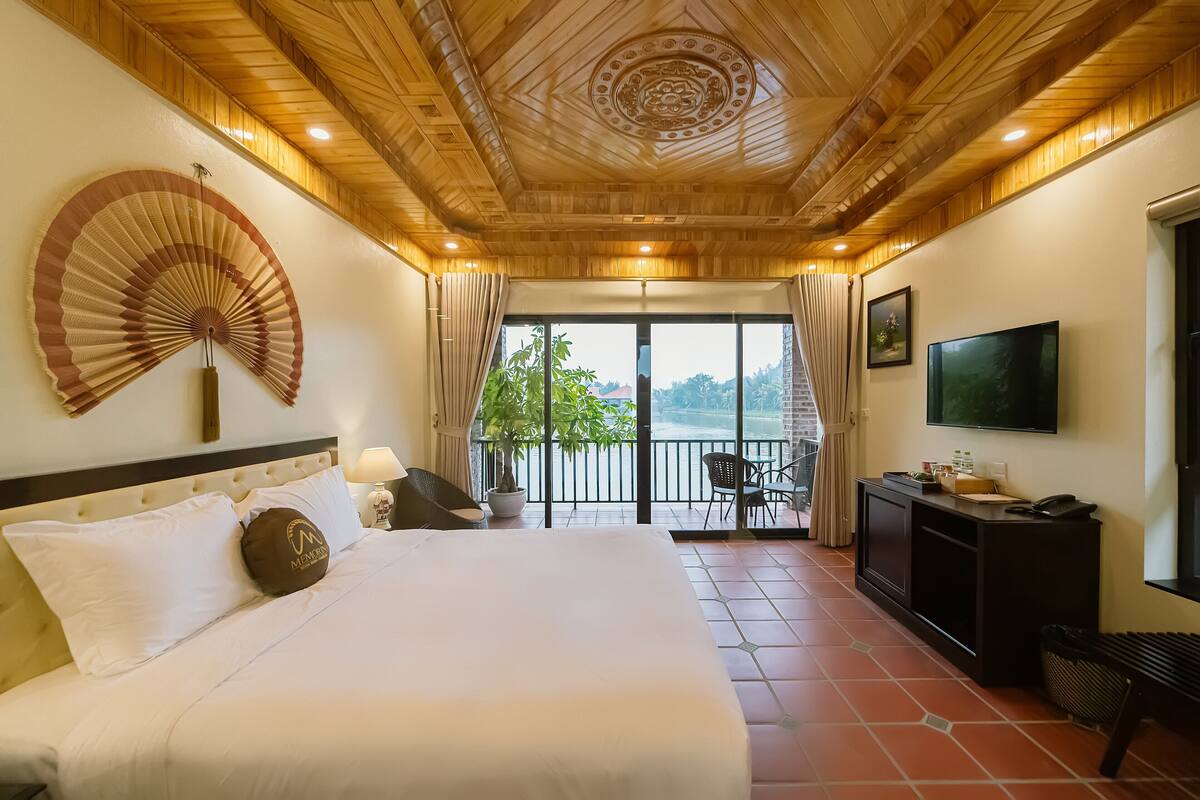 A hotel room with a large bed, a ceiling fan, a TV, and a balcony with a view.