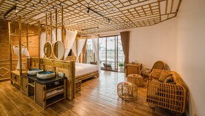 A room with a bed, two round mirrors, a vanity with a sink, wicker furniture, and a view through large windows. - Memorina Ninh Binh Resort (Tay Hoa Lu)