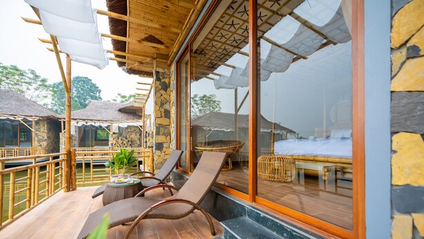 A balcony with wicker chairs, a table, and a view of a pool and other buildings. - Memorina Ninh Binh Resort (Tay Hoa Lu)