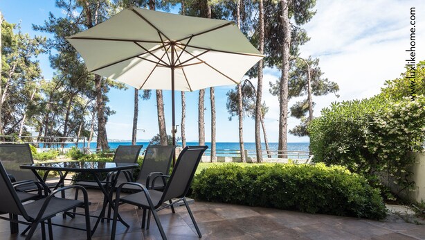 Um pátio externo com mesa e cadeiras, um guarda-sol grande e vista para o oceano.