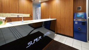 Un hall d'accueil d'hôtel avec un lambris en bois, un comptoir de réception, un kiosque bleu en libre-service et une enseigne indiquant « Super Hôtel ».