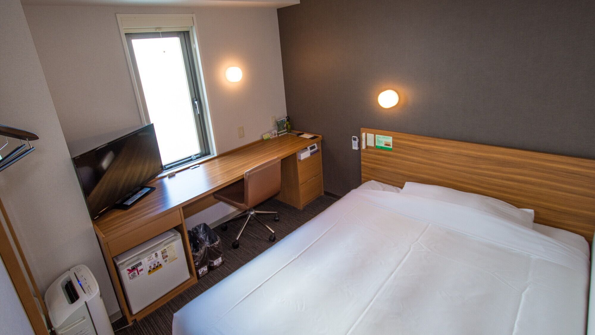 A hotel room with a bed, a desk with a computer, a TV, and a window.