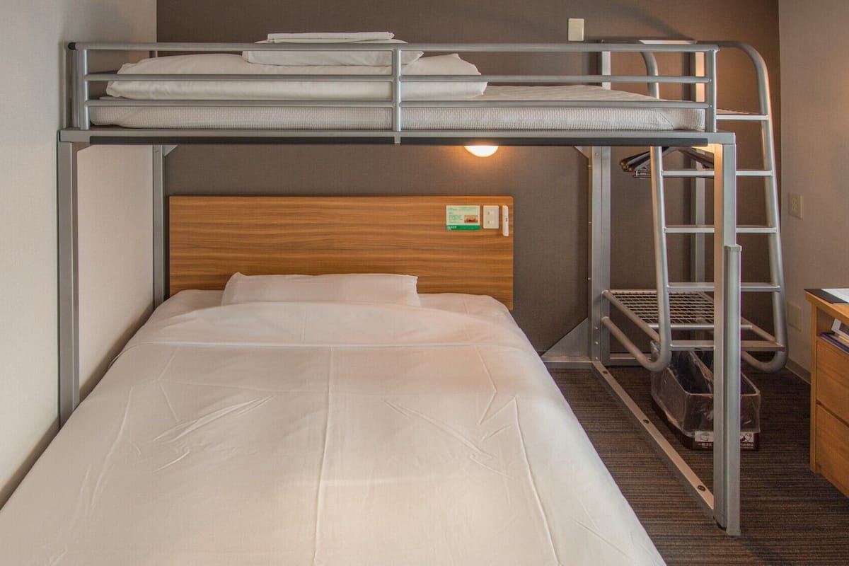 Een stapelbed met een bureau en een stoel, een houten hoofdbord en een wandlamp.