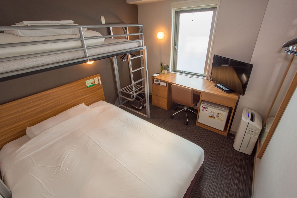 Een hotelkamer met een stapelbed, een bureau met een computer, een televisie en een raam.