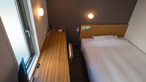 Une chambre d’hôtel compacte, dotée d’un bureau en bois, d’un lit simple et d’un petit coin salon.