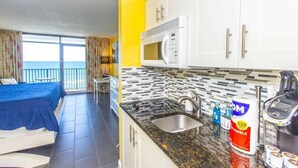Una habitación con cama, una mesa de comedor, una cocina equipada con microondas y pileta, y vista al océano.