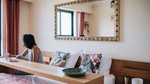 Une chambre d’hôtel avec un lit en bois, une table de chevet sur laquelle se trouve un bol, un miroir avec un cadre orné et une fenêtre avec des rideaux.