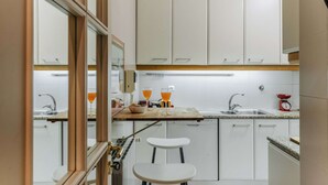 Une cuisine compacte avec des meubles blancs, un plan de travail en bois, un évier et un petit tabouret.