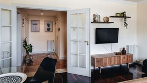 Un salon moderne avec une table basse en verre, un canapé en cuir noir, un meuble TV en bois et un téléviseur à écran plat fixé au mur.