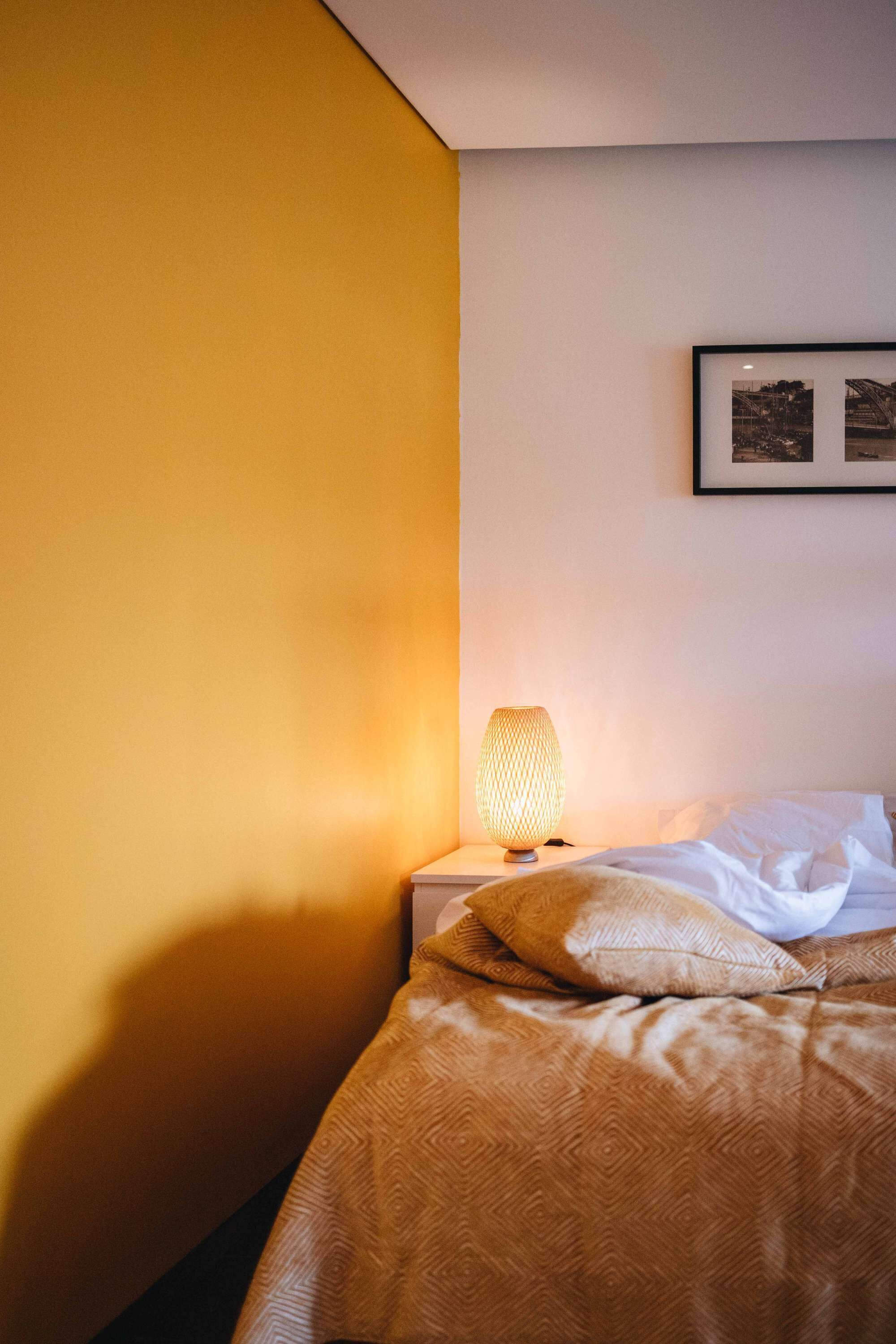 A neatly made bed with a patterned blanket and pillows, a bedside lamp, and a framed picture on the wall.